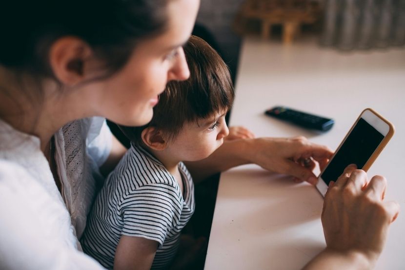 Mãe e filho, ambos com expressões focadas, olhando para um smartphone. O menino está ao lado da mãe, observando o que está na tela, enquanto ela segura o celular.