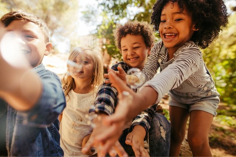 Crianças se divertindo ao brincar com bolhas de sabão no ambiente externo. A alegria e a interação entre os pequenos criam uma cena divertida e espontânea.