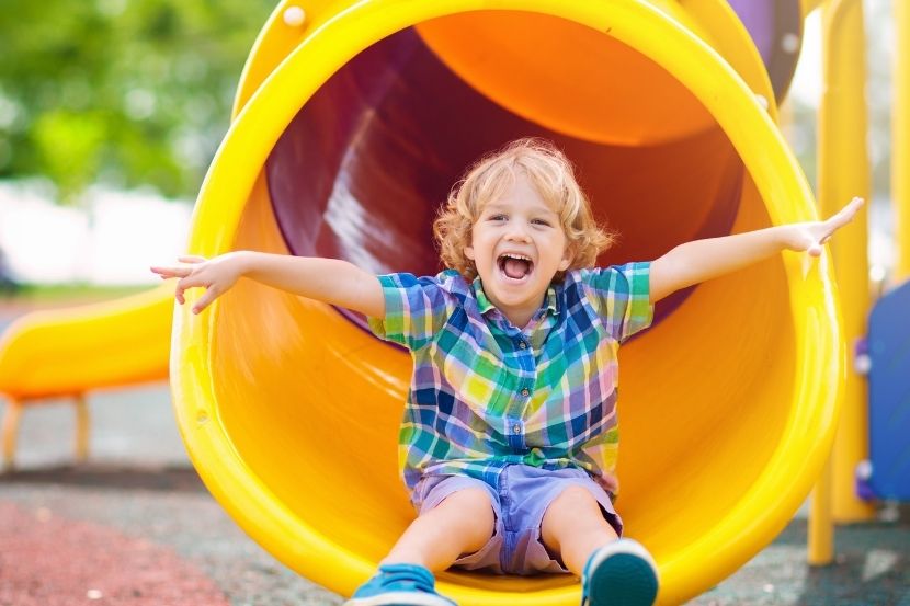 Menino se divertindo enquanto desce em um escorregador colorido no parquinho. Ele sorri com entusiasmo enquanto aproveita a brincadeira ao ar livre.