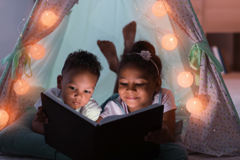 duas crianças lendo livro a noite na cabaninha