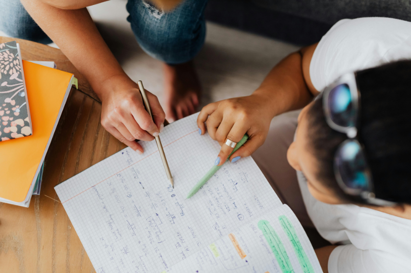 Sistemas de ensino que mais aprovam aluna tirando dúvida com professora com um cadernos em destaque