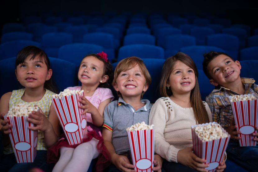 crianças de 5 anos assistindo filme no cinema com pipoca na mão