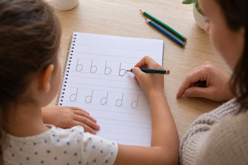 criança escreve letras espelhadas Criança pratica as letras b e d em um caderno de caligrafia